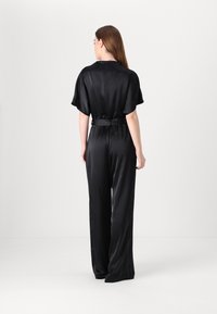 Svart sateng jumpsuit med korte pufferm, belte i midjen og vide bukser. Jevn tekstur, minimal detailing og avslappet passform.