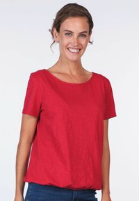 Red short-sleeve top with a round neckline, smooth texture, and gathered hem, paired with blue jeans.