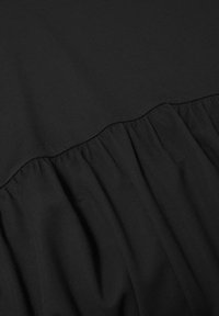 Tissu noir avec une couture froncée, texture lisse et léger brillant. Le matériau semble doux et léger.