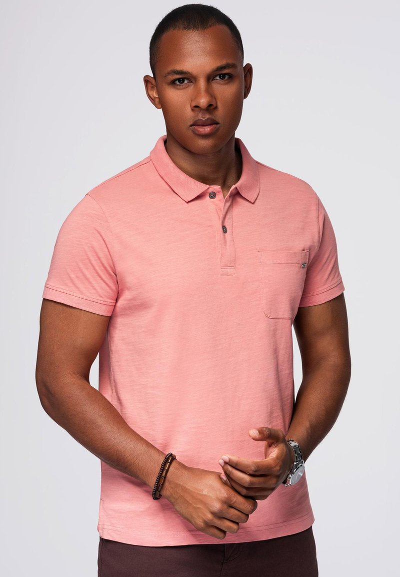 Svetle růžový polo tričko vyrobené z měkké látky, s límečkem, tříknoflíkovou légou a malou náprsní kapsou. Krátké rukávy a volný střih.