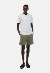 T-shirt en coton blanc, short vert olive, sandales noires ; design décontracté avec des manches courtes et des poches ; texture lisse sans motifs.