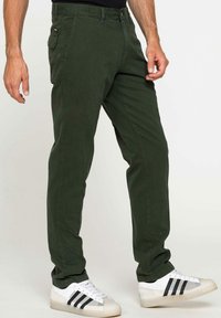 Pantaloni in twill di cotone verde scuro con vestibilità slim, dotati di chiusura a bottoni e tasche laterali, abbinati a sneaker bianche.
