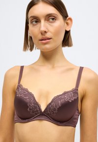 Gilus mauvės spalvos liemenėlė su nėrinių apdaila ant kaušelių ir reguliuojamomis petnešėlėmis. Lygus paviršius su subtiliai suformuota forma.