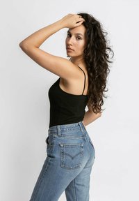 Zwarte tanktop en blauwe hoge taille spijkerbroek. De spijkerbroek heeft achterzakken en een merklabel op de tailleband. Kruidachtig haar.