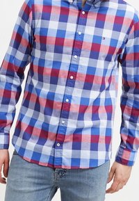 Kariertes Hemd in Blau, Rot und Weiß; durchgeknöpftes Design mit langen Ärmeln. Weiche Textur und deutlich sichtbare Muster über die gesamte Fläche.