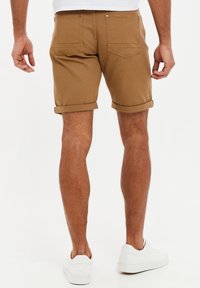 Shorts marrones con puños enrollados y una textura en la tela, que presentan dos bolsillos traseros y detalles de costura mínimos, combinados con zapatillas blancas.
