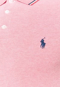 Polo shirt in een roze textuurstof, met een marineblauw logo en witte en marineblauwe gestreepte kraagaccenten, met opvallende knopen.