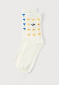 Hvite knelangs sokker med blomsterpattern: blå tulipaner på den ene siden, gule blomster på den andre, med en svart logo. Jevn tekstur.