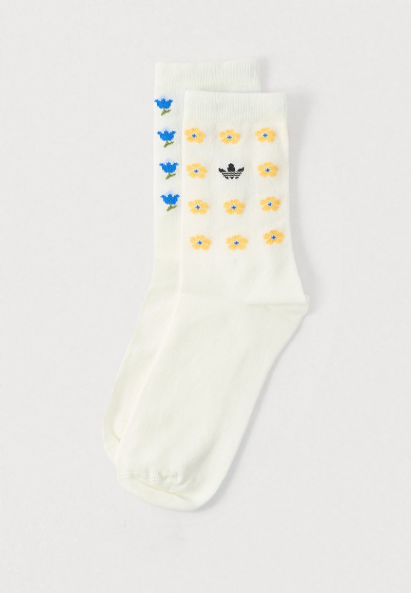 White knee-length socks with floral patterns: blue tulips on one side, yellow flowers on the other, with a black logo. Smooth texture.