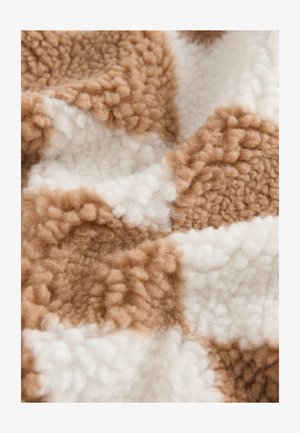 Bruin-wit geblokt stof met een pluizig, getextureerd oppervlak. Het patroon bestaat uit afwisselende vlakken van zacht, pluizig materiaal.