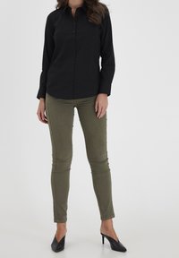 Black button-up shirt with collar, long sleeves; fitted olive green pants; black high heels; smooth texture, casual design.