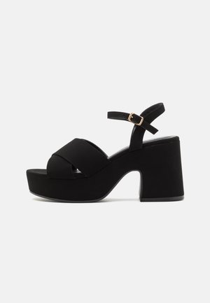 Black platform sandals with a wide front strap and adjustable ankle strap. Made of smooth material with a block heel and a rounded toe.