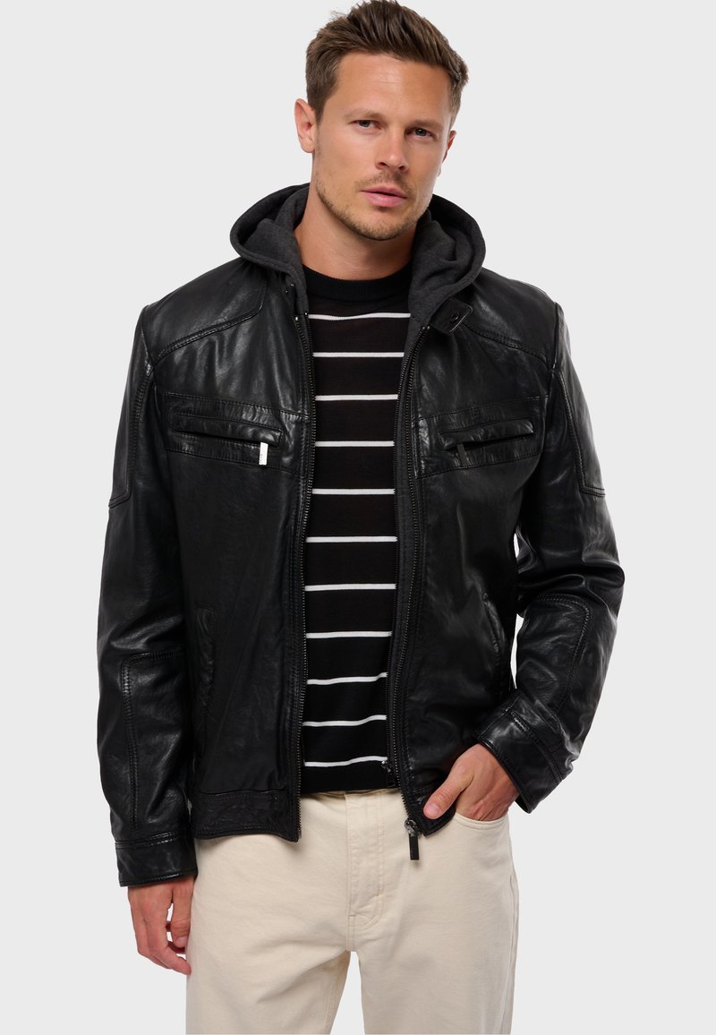 Chaqueta de cuero negra con frontal con cremallera, dos bolsillos en el pecho y un forro de sudadera gris. Llevada sobre un suéter a rayas en blanco y negro.