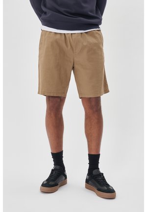 Shorts en coton beige avec une taille élastique, longueur genou, associés à des baskets noires et des chaussettes de cheville noires. Design simple, sans motifs.