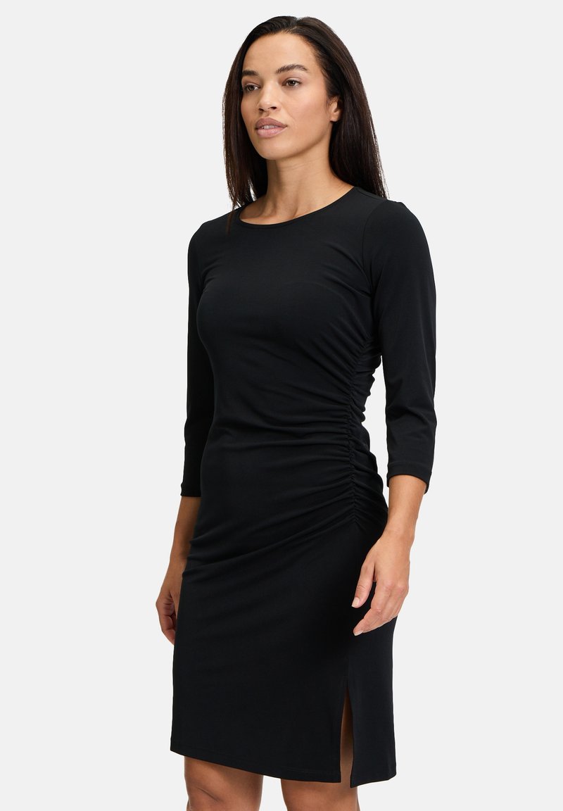 Schwarzes Kleid mit einem runden Ausschnitt und Dreiviertelärmeln. Verfügt über seitliche Raffung und einen Schlitz bis zum Oberschenkel für zusätzlichen Detail. Glatter Stoff.