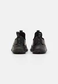 Schwarze Sportschuhe mit glatter Oberfläche, die ein niedriges Profil aufweisen, strukturierte Sohlen und Ziehtabs an der Ferse für einfaches Anziehen.