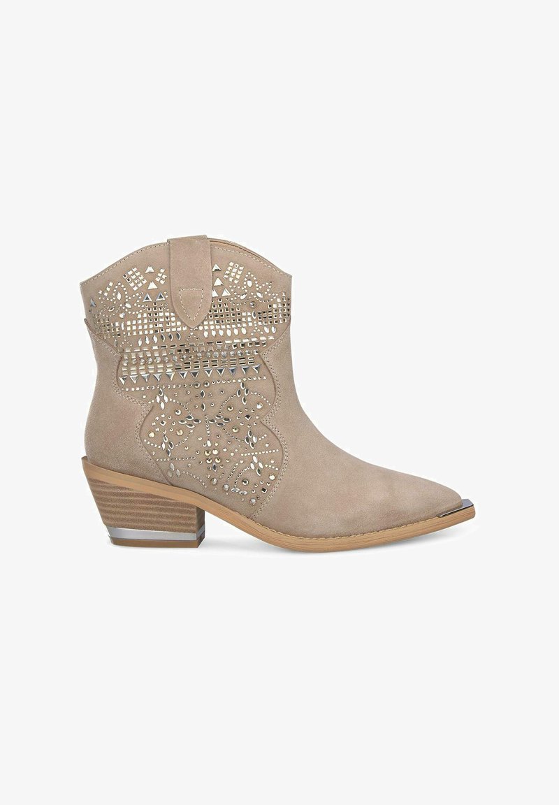 Stivale ankle in suede beige con punta affusolata, motivo a borchie argentate e tacco impilato. Presenta perforazioni decorative e un design a scallop.