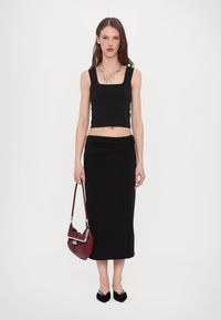 Black cropped tank top and high-waisted draped skirt, paired with a burgundy handbag. Model wears pointed black flats and a chunky necklace.