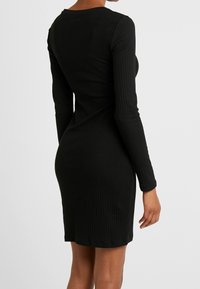 Svart ribbad långärmad klänning med en figurnära silhuett, rund halsringning och knälång längd, med ett strukturerat tyg.