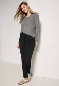 Grijze V-hals trui en zwarte jogpants met een trekkoord. Lichtcrème sneakers met grijze accenten en een gestructureerde afwerking.