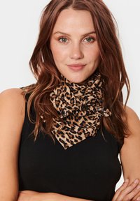 Leopardprint tørklæde i blødt stof, med en bundet knudedesign, i farverne beige og sort, båret med en sort top.