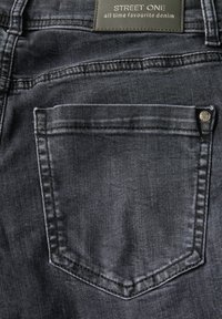 Jeans de mezclilla gris oscuro que presentan un bolsillo trasero con un borde cosido y una pequeña tachuela metálica. La etiqueta dice "STREET ONE" en texto blanco.