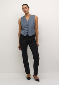 Gilet grigio a righe sottili senza maniche con scollatura a V e cinque bottoni neri, abbinato a pantaloni neri slim e scarpe nere a punta.