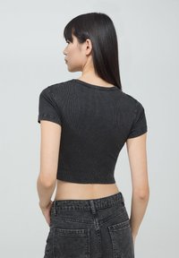 Top corto a coste nero con maniche corte, scollatura rotonda e design aderente. Abbinato a jeans in denim neri a vita alta.