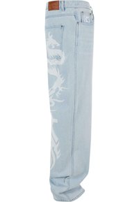 Vaqueros de mezclilla azul claro con un gran gráfico de dragón blanco a lo largo del lado izquierdo y una etiqueta de piel marrón con la marca en la parte trasera de la cintura.