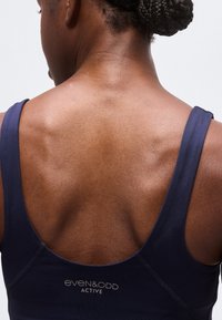 Vue arrière d’une personne aux cheveux tressés portant un débardeur de sport Even&Odd Active bleu marine.