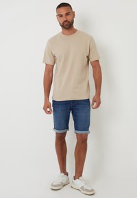 T-shirt beige con collo a giro, maniche arrotolate, abbinato a pantaloni shorts di denim con orli risvoltati. Indossato con sneakers bianche con dettagli grigi.