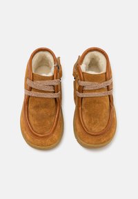 Chaussures en suède marron avec un bord en cuir lisse, des lacets texturés et une doublure intérieure douce. Forme arrondie avec une semelle en caoutchouc.