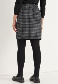 Graue karierte Minirock mit taillierte Passform, strukturiertem Stoff und Rückenfalten. Kombiniert mit schwarzen Strumpfhosen und schwarzen Slippers.