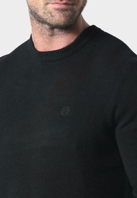 Czarny sweter z dzianiny z prążkowanym okrągłym dekoltem, z delikatnie wytłoczonym logo na piersi, charakteryzujący się gładką teksturą.