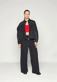 Svart vindjakke med hvite detaljer, rød crop top og løse svarte bukser. Glatt tekstur, avslappet passform, atletisk design.