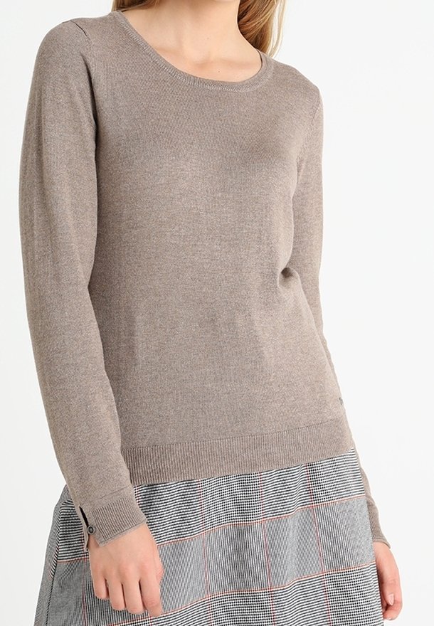 Femme portant un pull taupe à manches longues et col rond, associé à une jupe grise à carreaux avec de fines lignes rouges.