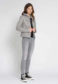 Grijze leren jas met een afneembare grijze hoodie, ritssluiting aan de voorkant, twee zijzakken, gecombineerd met gescheurde grijze spijkerbroek en zwarte hoge sneakers.