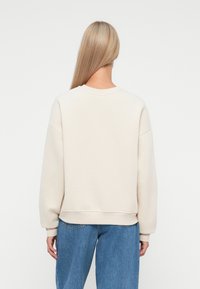 Lichtbeige sweatshirt met een ronde hals, verlaagde schouders en geribde manchetten, gecombineerd met losse blauwe jeans. Zachte stoftextuur.