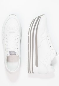Baskets de sport blanches avec une tige en cuir lisse, des détails perforés, une semelle rayée grise et un design à lacets.