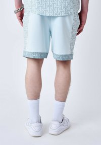 Shorts bleu clair avec un motif géométrique, taille élastique et bande décorative au bas ; portés avec des chaussettes de sport blanches et des chaussures.