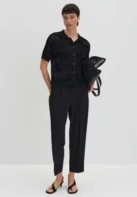Schwarzes kurzärmeliges Hemd mit Knopfleiste und strukturiertem Muster, kombiniert mit maßgeschneiderten schwarzen Hosen und schwarzen Sandalen mit offenen Zehen. Schwarze Tasche inklusive.