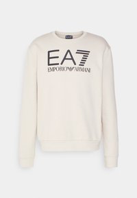 Béžová mikina s kulatým výstřihem a dlouhými rukávy. Na přední straně je černé grafické logo „EA7 EMPORIO ARMANI“. Hladká textura.