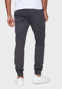 Gray jogger pants feature a tapered design with elastic cuffs, back pockets, and a smooth texture, paired with white sneakers.