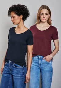 Due magliette a maniche corte: una in blu navy con scollatura ampia, l'altra in bordeaux con scollatura standard, abbinate a jeans blu.