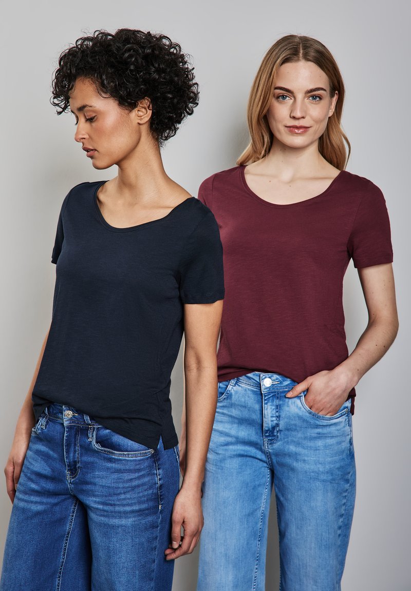 Due magliette a maniche corte: una in blu navy con scollatura ampia, l'altra in bordeaux con scollatura standard, abbinate a jeans blu.