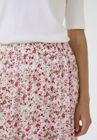 Blumenrock aus leichtem Stoff, mit einem weißen Hintergrund und roten sowie grünen Blumen. Elastischer Bund und gefältetes Design.