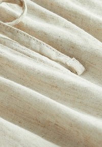 Slonovinový materiál s texturovanou vazbou, obsahující jemné záhyby a malou smyčku na okraji. Neutrální barva s jemnými skvrnami.