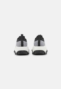 Schwarz-weiße Sportschuhe mit einem geflochtenen Obermaterial, strukturiertem Stoff und dicker Gummisohle. Verfügt über einen Schlupfgriff und kontrastierende Akzente.