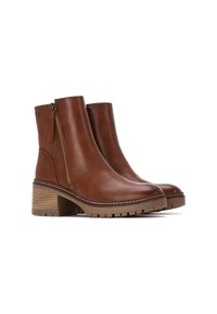 Botas de tobillo de cuero marrón con tacón grueso, cremallera lateral y suela de goma texturizada que presenta ranuras horizontales y un borde cosido.
