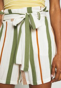 Shorts rayés en blanc, vert et orange. Fabriqués en tissu léger. Dotés d'une ceinture à nouer à l'avant et d'un design décontracté.